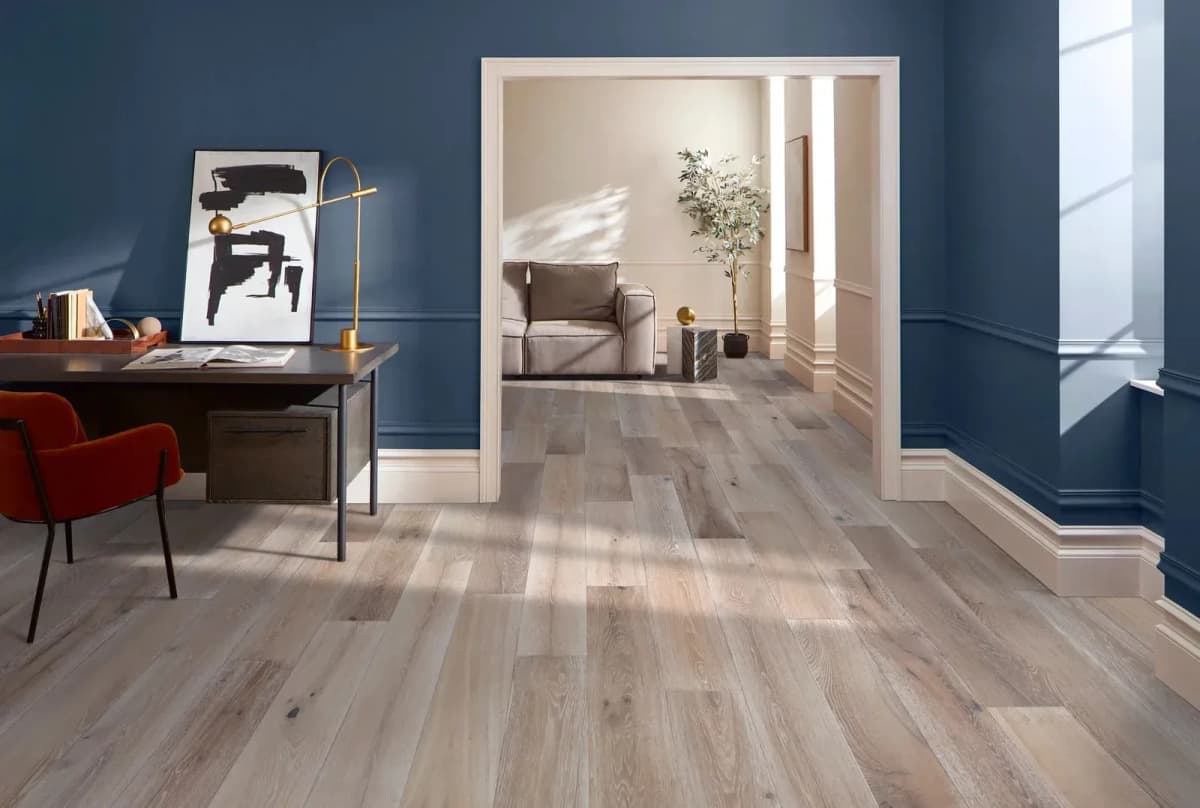 Anderson Tuftex Tidepool white oak flooring runs from a blue home office through an open doorway into a living room.