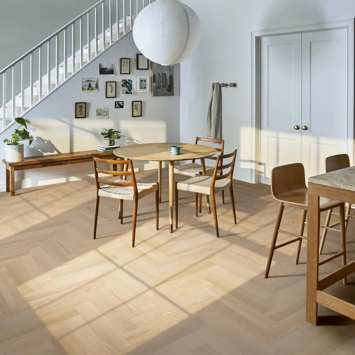 European ash engineered hardwood laid in a herringbone pattern across a sunlit dining area with a round table and staircase