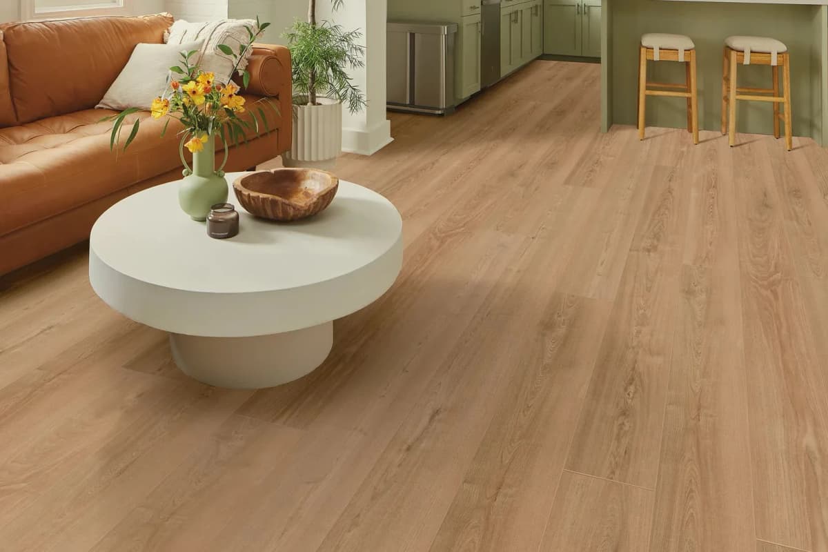Antique Chestnut luxury vinyl plank flooring in a living room with a cognac leather sofa, a round white coffee table and two counter stools