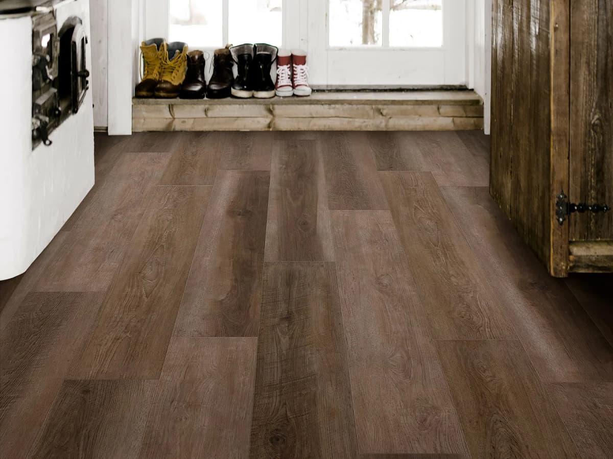 Warm brown wood-look luxury vinyl plank flooring in a farmhouse entryway, with boots and kids' sneakers lined up by the door