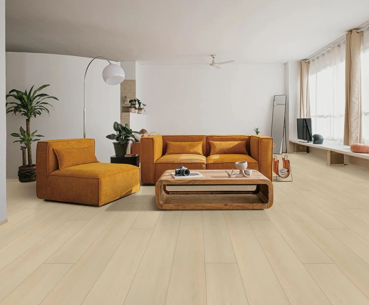Light cream oak-look luxury vinyl plank flooring in a bright, minimalist living room with a mustard sectional sofa and floor-to-ceiling windows