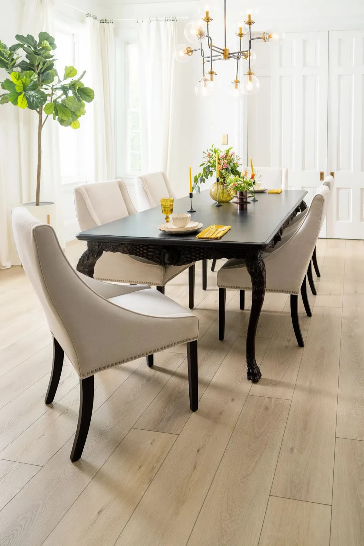 A dark dining table with carved legs and upholstered chairs on light oak luxury vinyl plank flooring