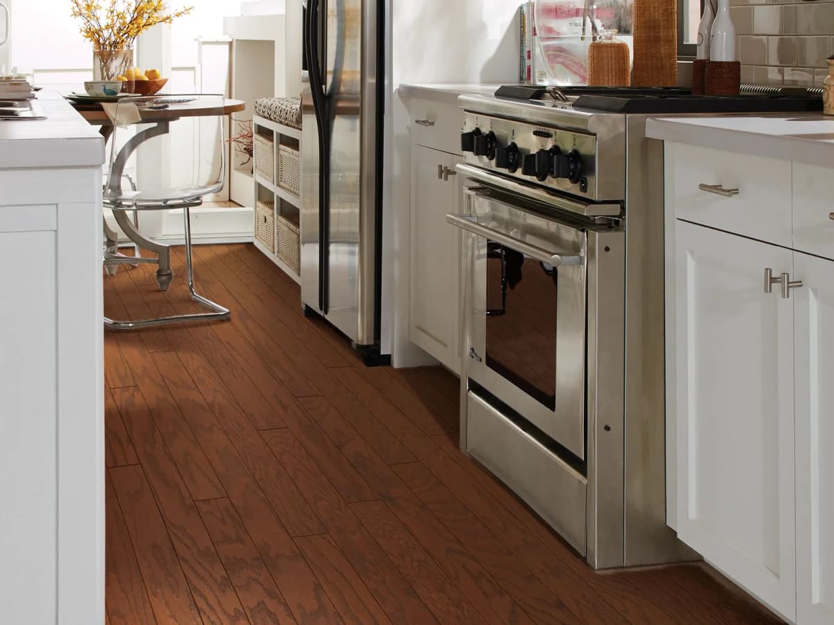 Reddish-brown engineered hardwood flooring in a kitchen with white cabinetry and a stainless steel range