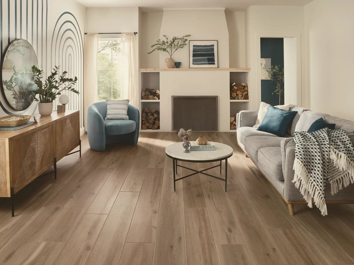 COREtec Originals Premium luxury vinyl plank in Parchment Oak in a bright living room with a gray sofa, blue accent chair and a plastered fireplace with built-in firewood niches