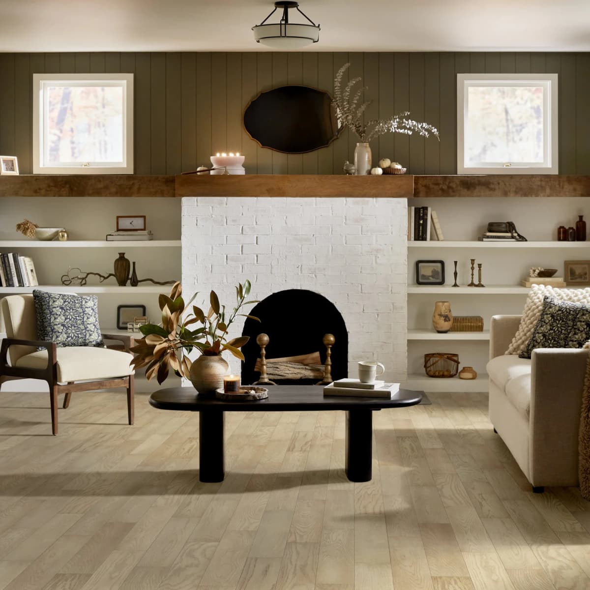Light white oak engineered hardwood flooring laid in straight staggered planks anchors a styled living room with a painted brick fireplace and built-in shelving