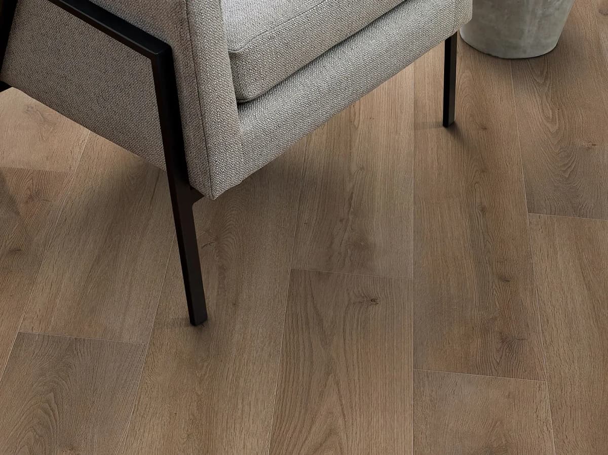 Close-up of wood-grain textured luxury vinyl plank flooring beside a chair leg, showing the realistic detail of the surface finish