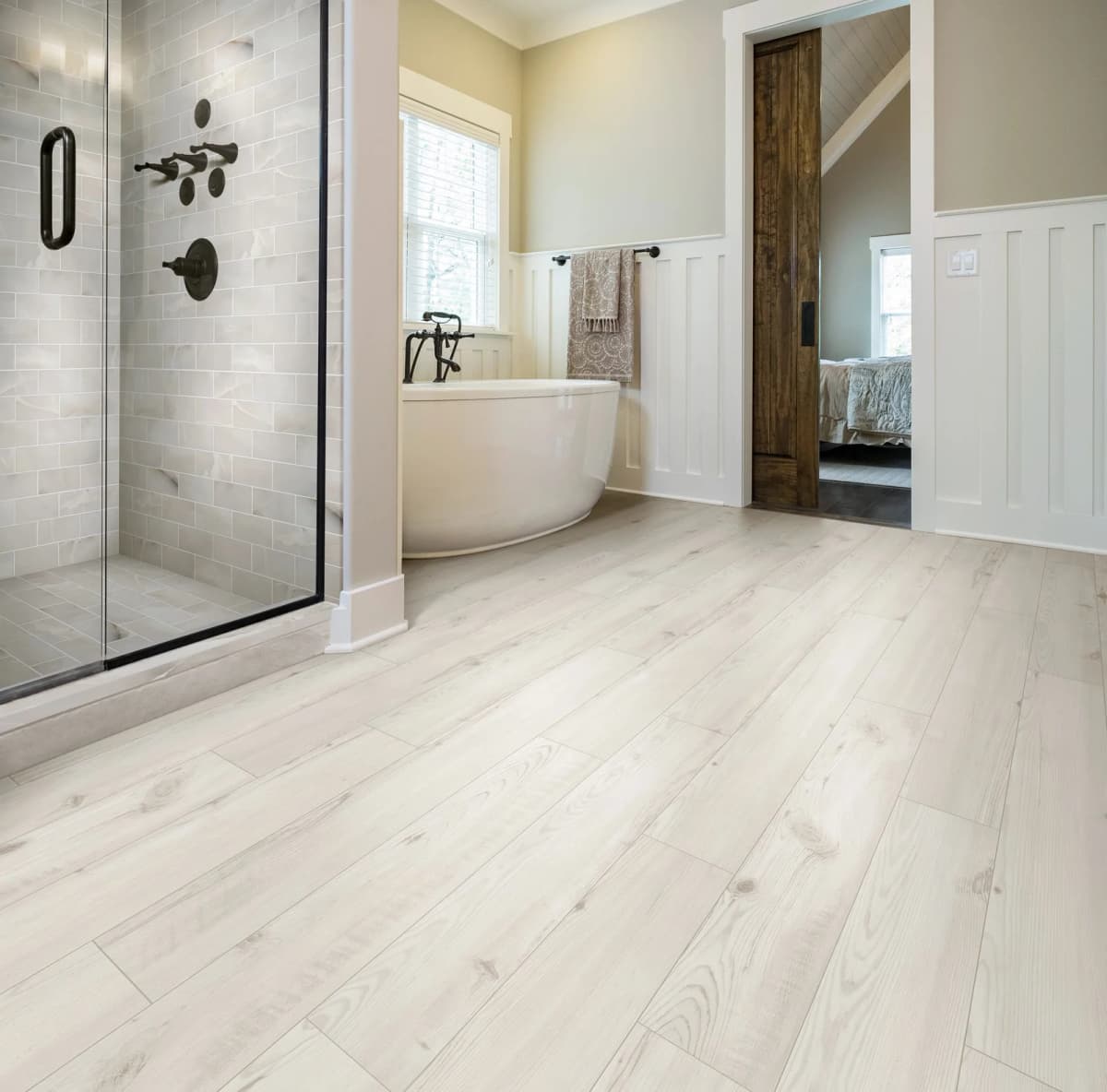 Pale wood-look luxury vinyl plank flooring running through a bright bathroom with a soaking tub and glass-enclosed walk-in shower