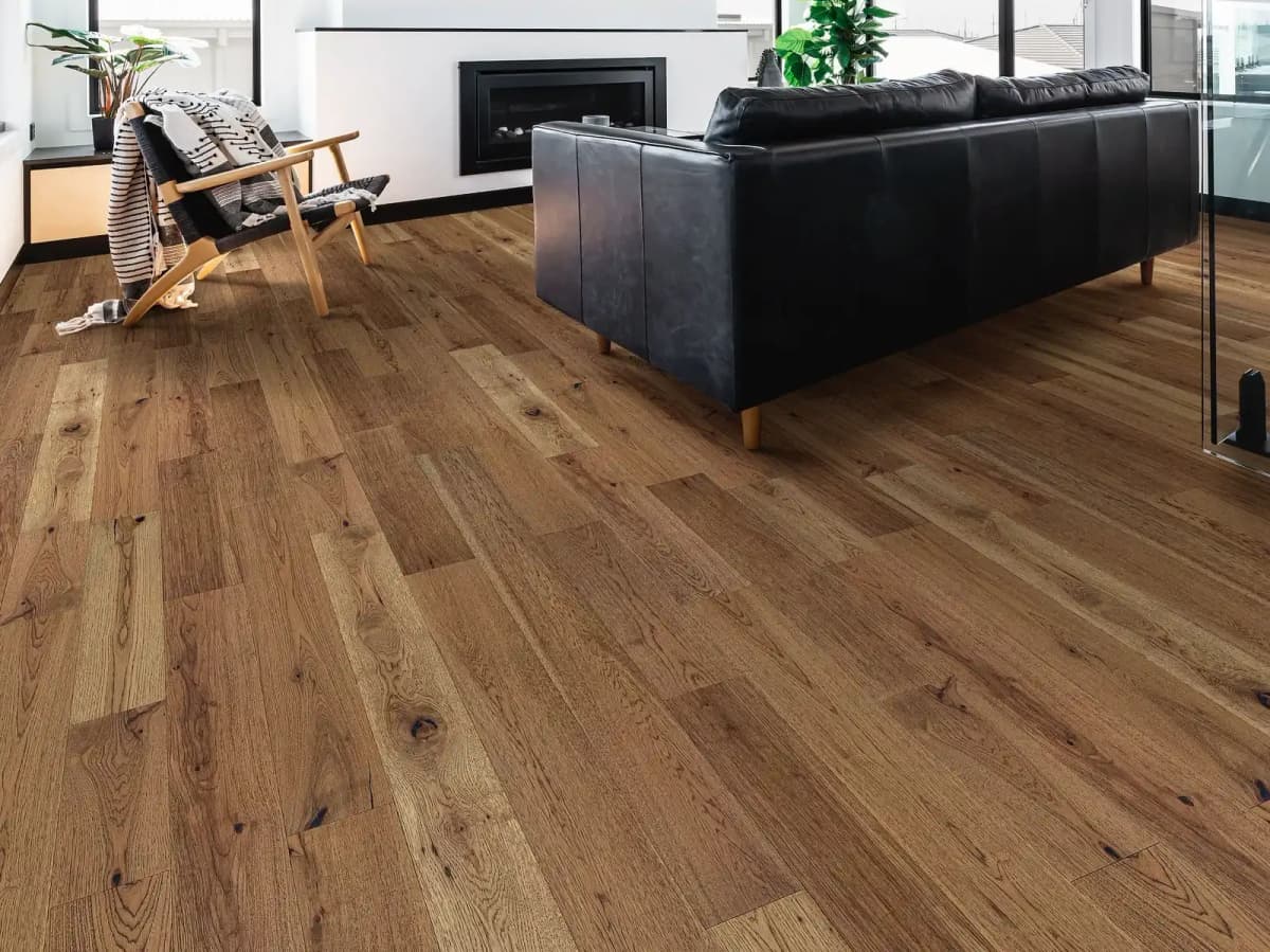 Warm wheat-toned pecan hardwood floor in a staggered plank layout filling a modern living room with a black leather sofa and fireplace