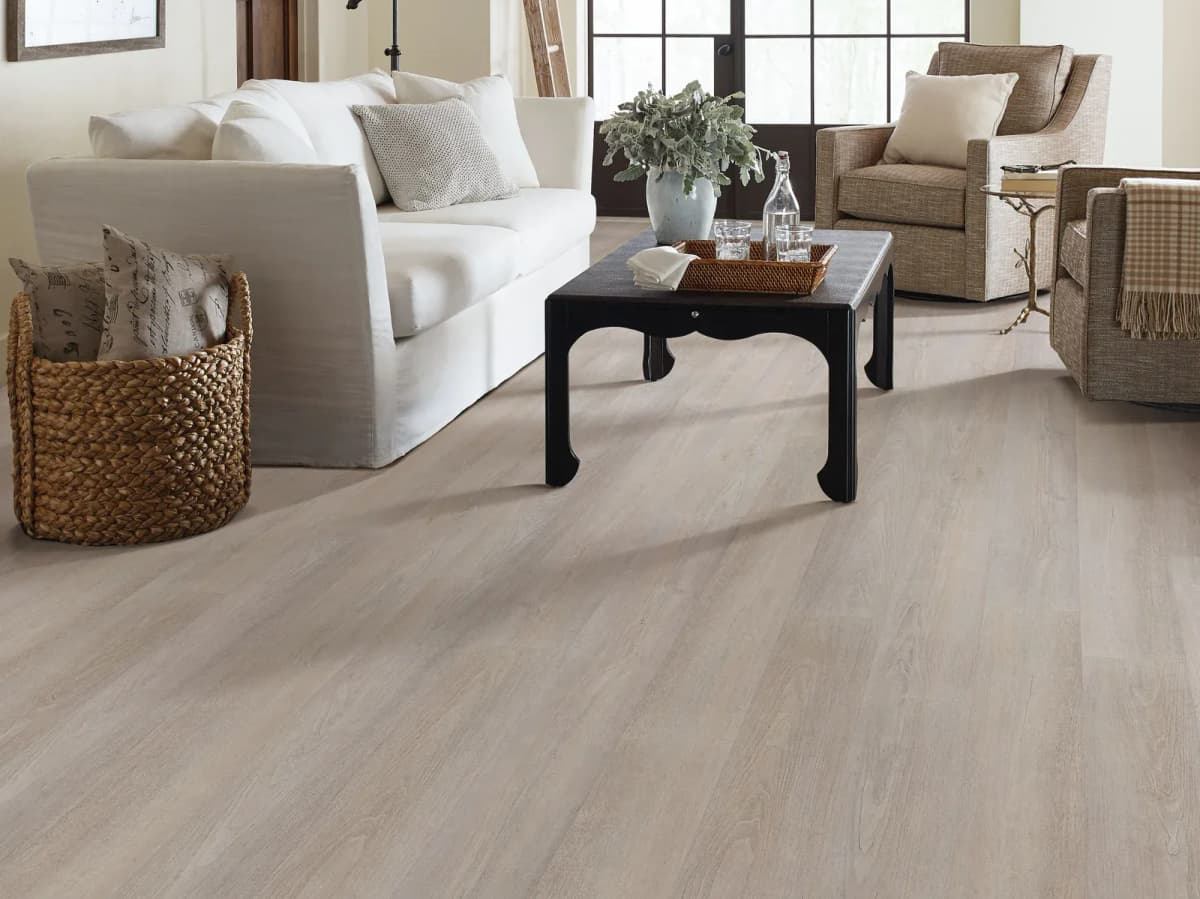 Greige Walnut luxury vinyl plank flooring in a living room with a white slipcovered sofa, a low black table, and two woven armchairs