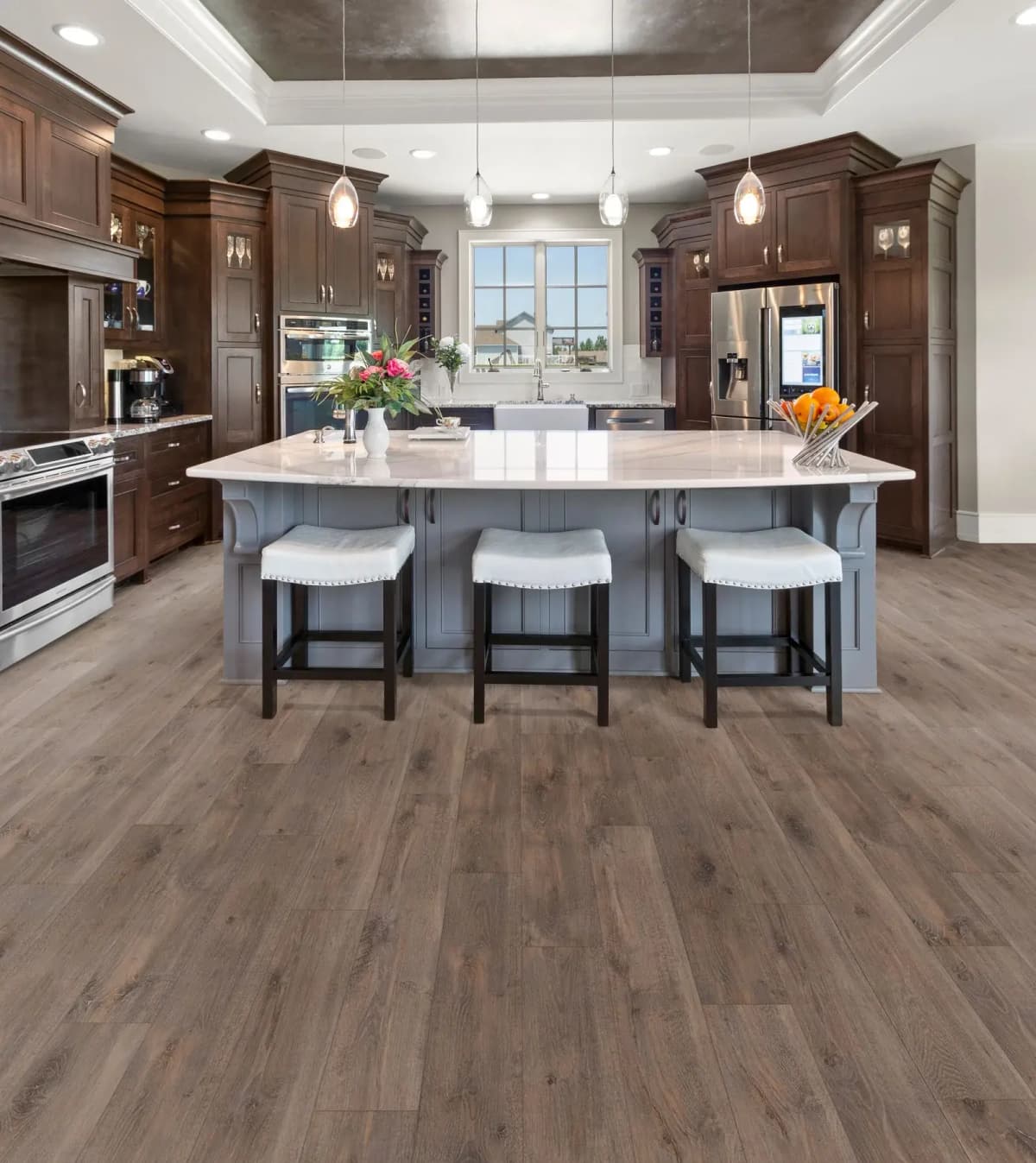Dark wood-look luxury vinyl plank flooring filling a large kitchen with a gray island, barstools, and stainless steel appliances