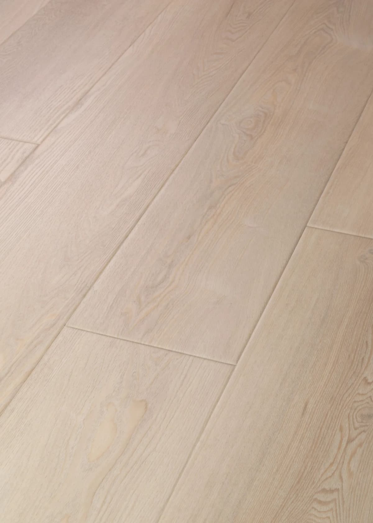 Close-up of light Conch Ash luxury vinyl plank flooring showing embossed wood grain texture and a plank seam under soft, even lighting