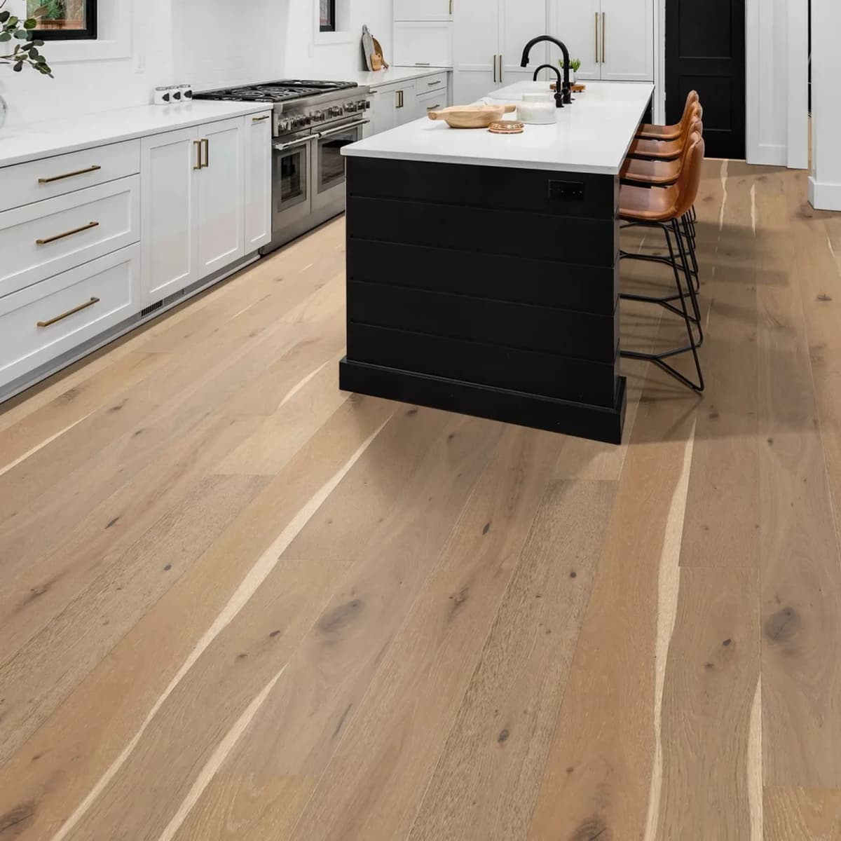 Alla Prima white oak engineered planks run wide across a bright kitchen with white cabinetry and a black island.