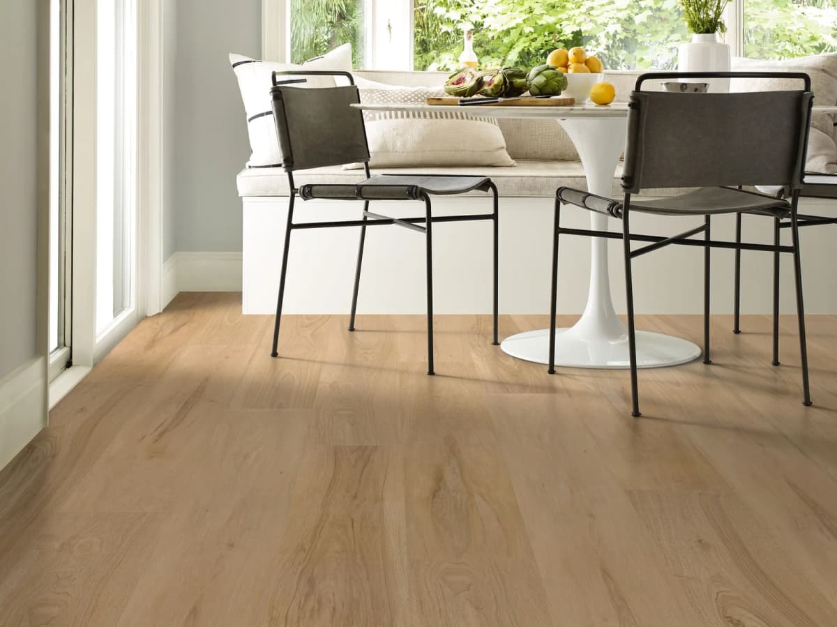 Light tan luxury vinyl plank flooring in a sunroom breakfast nook with a built-in bench, black metal chairs, and floor-to-ceiling windows facing greenery