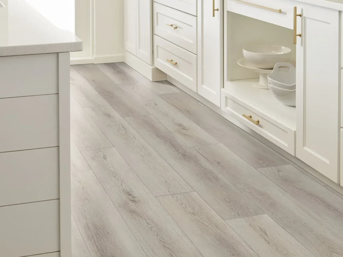 Warm Grey luxury vinyl plank flooring installed in a bright kitchen with white cabinetry and brass hardware