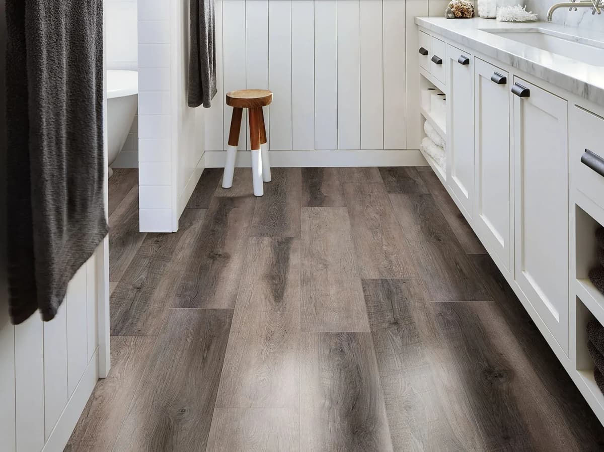 Gray wood-look vinyl plank flooring across a bright bathroom with white cabinetry