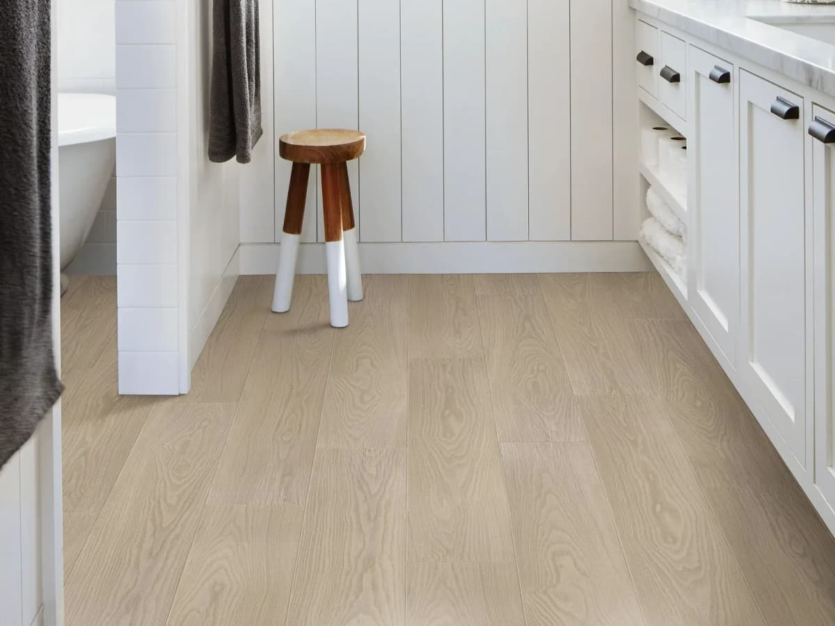 Light wood-look vinyl plank flooring in a bathroom with white cabinetry and a wood stool