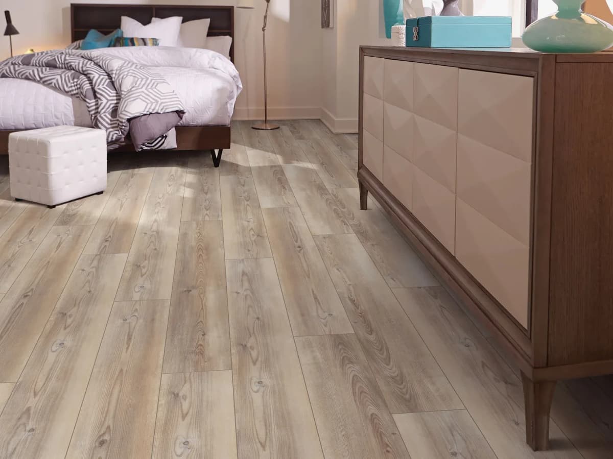 Light gray-beige luxury vinyl plank flooring in a bedroom with a dark wood bed.