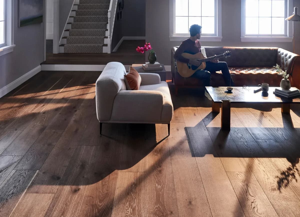 Warm brown white oak plank flooring runs from a staircase with a patterned runner into a sunlit living room.