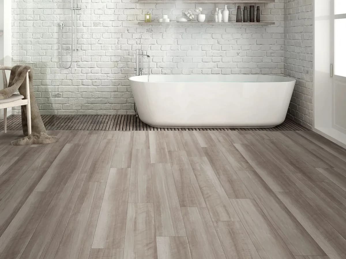 Gray luxury vinyl plank flooring with a freestanding tub fills a bright bathroom.