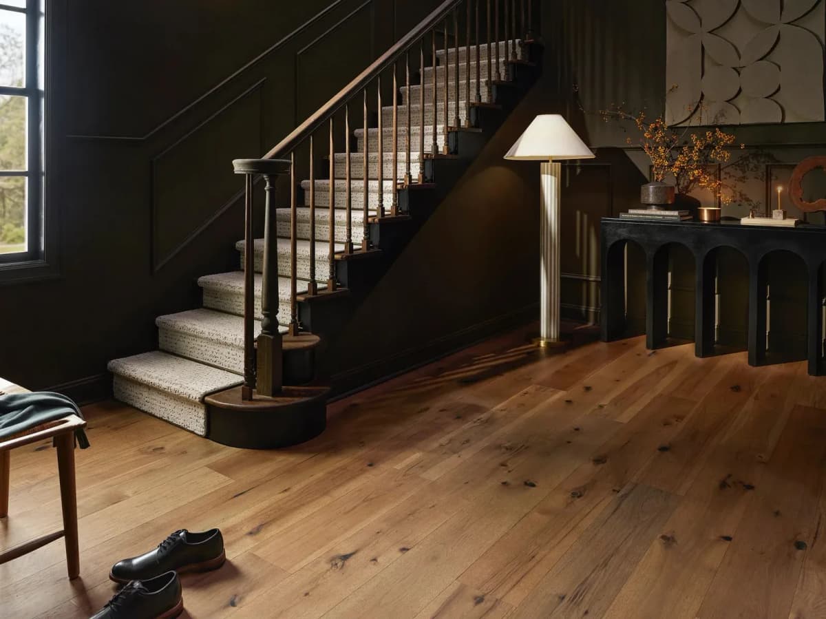 Anderson Tuftex wide-plank hickory flooring in a warm amber tone fills a dark panelled entryway with a staircase.