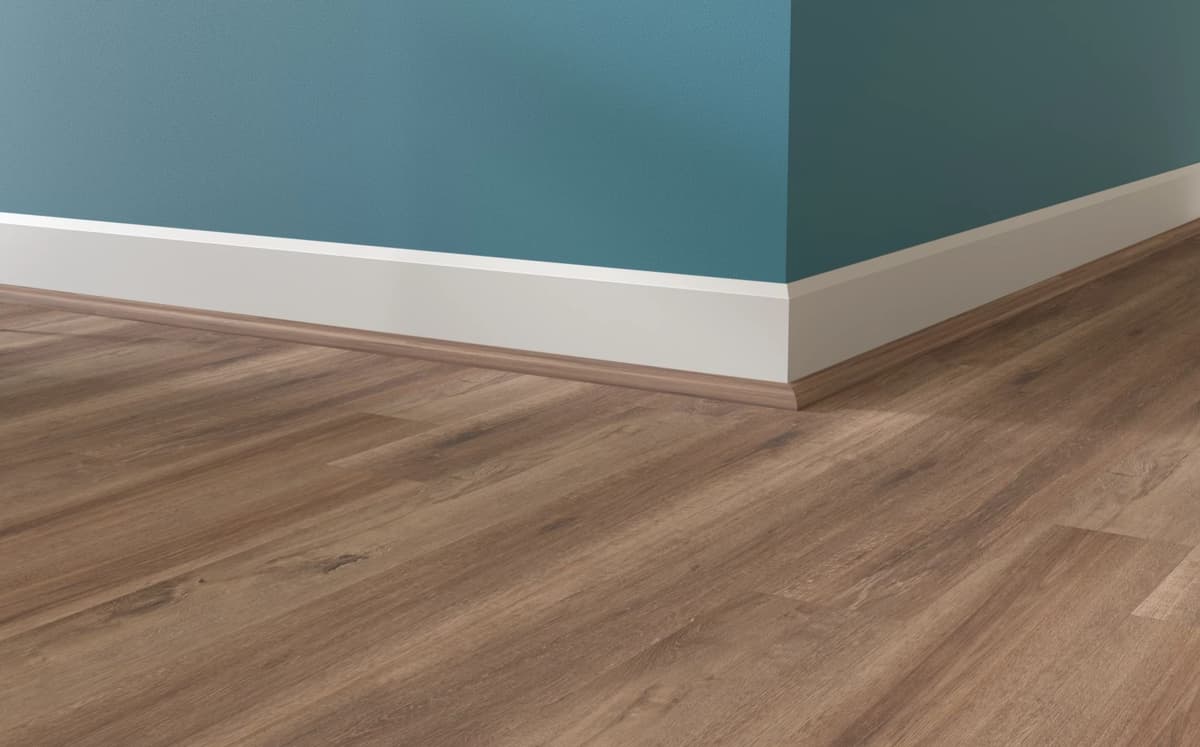 Wood-tone quarter round tucked against a white baseboard, covering the expansion gap where the plank floor meets the wall